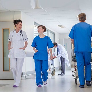 Medizinisches Personal geht durch Flur, im Hintergrund wird ein Patient versorgt.