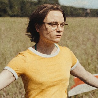 Szene aus dem Film „In die Sonne schauen“: Ein Mädchen läuft mit zwei Fahnen in der Hand durch ein Feld.