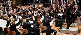 Orchester spielt unter Leitung eines Dirigenten im Konzertsaal.