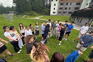 Jugendliche stehen im Kreis auf einer Wiese und halten ein gespanntes Seil.