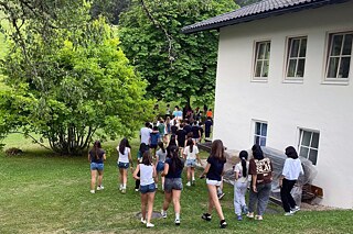 Jugendliche laufen um ein Gebäude, dahinter ist ein Wald zu erkennen.