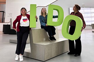 Three young women are holding up the letters I, D and O and laughing happily.