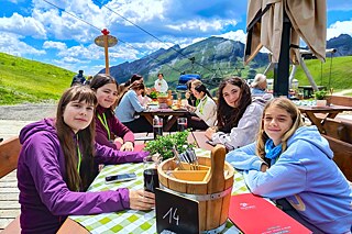 Jugendliche sitzen an langen Tischen auf einer Alm.