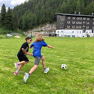 Zwei Jungen laufen auf einer Wiese einem Fußball hinterher.