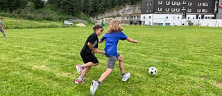Zwei Jungen laufen auf einer Wiese einem Fußball hinterher.