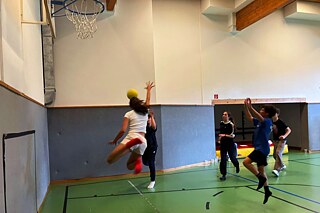Jugendliche spielen Basketball in einer Sporthalle.
