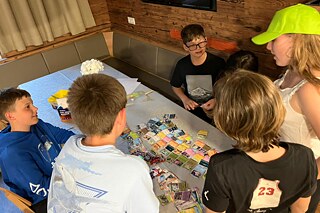 Jugendliche sind um einen Tisch versammelt und blicken auf kleine Sammelkarten.