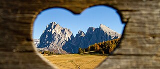 Blick auf die Dolomiten durch ein Herz, dass in ein Holzbrett eingearbeitet ist.