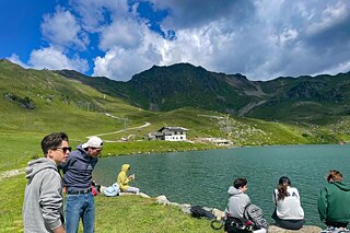Jugendliche stehen am Ufer eines Sees und bewundern die Landschaft.