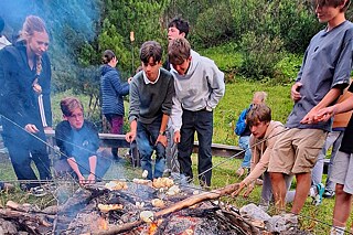 Jugendliche halten Stöcke mit Marshmallows über ein offenes Holzfeuer.