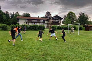 Jugendliche spielen Fußball auf einer Wiese.