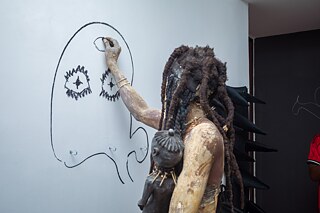 Performance-Künstler mit skulpturalem Kostüm an einer partizipativen Kunstwand bei der Ausstellung „Elima-NoBody“ im Musée d'Art Contemporain et Multimédia in Kinshasa.