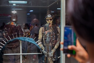 Ein Performance-Künstler betrachtet ein Exponat in einem Glaskasten in der Ausstellung „Elima-NoBody“ im Musée d'Art Contemporain et Multimédia in Kinshasa.