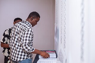 Besucher lesen Dokumente und Ausstellungstexte an einem Präsentationstisch in der Ausstellung „Elima-NoBody“ im Musée d'Art Contemporain et Multimédia in Kinshasa.
