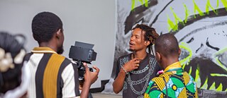 Besucher:innen im Gespräch während der Vernissage von Elima - NoBody vor einem großformatigen Kunstwerk in Schwarz, Grau und Neongrün.