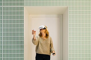 a blonde woman in a tiled room with a VR headset and a controller in her hand