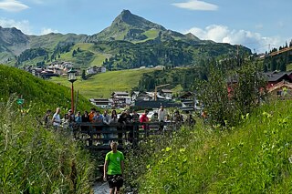 Jugendliche auf einer Holzbrücke beobachten ihre selbst gebastelten Flöße im Bach.