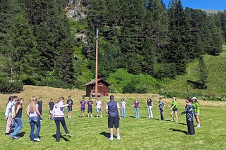 Jugendliche stehen in einem großen Kreis auf einer Wiese.
