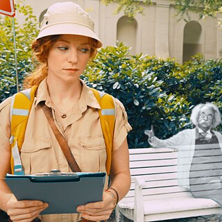 Filmszene aus „Cleo“: Junge Frau mit Schreibmappe, neben einer transparenten Einstein-Figur auf einer Parkbank.