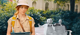 Filmszene aus „Cleo“: Junge Frau mit Schreibmappe, neben einer transparenten Einstein-Figur auf einer Parkbank.