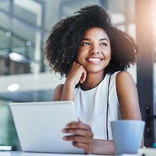 Eine Geschäftsfrau arbeitet im Büro mit Tablet und Laptop. Sie lächelt glücklich.