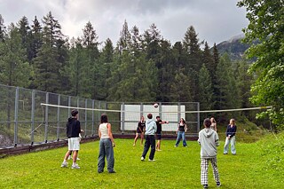 Jugendliche spielen Volleyball auf einer Wiese in den Bergen.