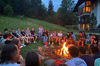 Jugendliche sitzen um ein offenes Feuer und singen.
