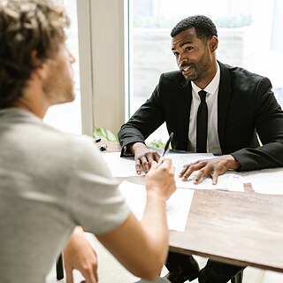 Two people sit at a table discussing notes and documents.