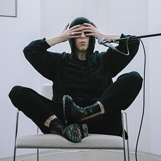 L'artista Eszter Salamon in una scena di Dance for Nothing (revisited), seduta su una sedia con le mani davanti al volto.