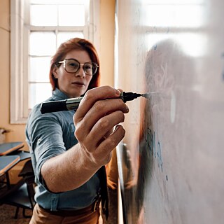 Portrait einer Frau, die mit einem Marker am Whiteboard schreibt.