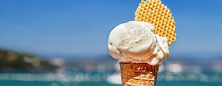 vor Meer hält eine Hand ein Eis in der Waffel