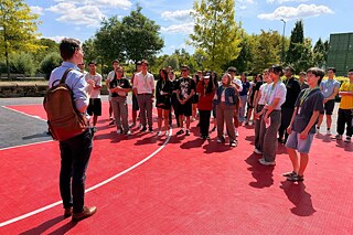 Jugendliche lauschen der Ansprache eines Erwachsenen auf einem Sportplatz.