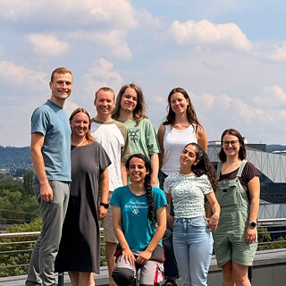 Eine kleine Gruppe auf einem Dach grüßt in die Kamera.