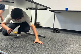Jugendliche krabbelt unter einem Tisch durch, auf einem Suppenlöffel balanciert er ein gefärbtes Ei.