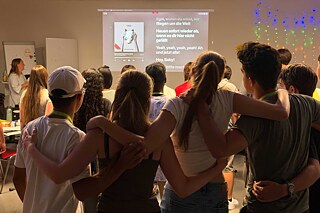 Jugendliche singen ein Lied, dessen Text auf einer großen Leinwand eingeblendet ist.