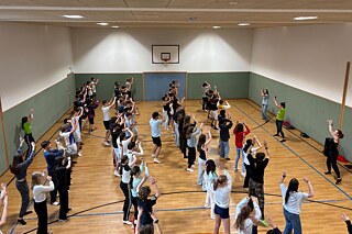 Jugendliche tanzen in einer großen Sporthalle.