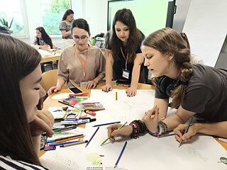 Учасниці академії працюють у групі над спільним плакатом, обговорюючи ідеї та візуалізуючи результати своєї проєктної роботи.