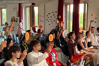 Jugendliche in einem Raum halten Abstimmungskarten in die Höhe.