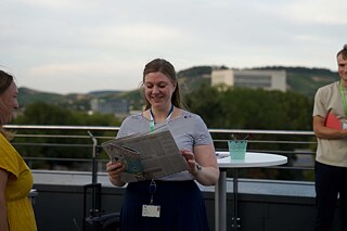 Junge Frau hält eine Zeitung in der Hand und ist sichtlich angetan.
