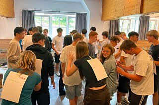 Jugendliche schreiben auf Zettel, die am Rücken anderer Jugendlicher kleben.