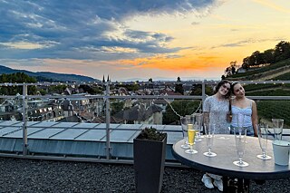 Zwei junge Frauen auf einer Dachterrasse bei Sonnenuntergang.