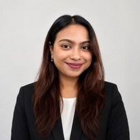 Portrait photo of a person in formal business attire, facing the camera against a plain light-gray background with a professional headshot composition.