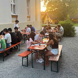 Jugendliche sitzen an langen Biertischen und basteln.