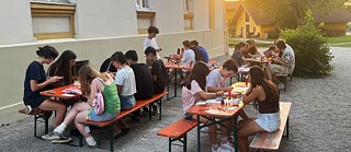 Jugendliche sitzen an langen Biertischen und basteln.