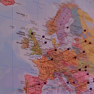L’image montre un extrait d’une carte imprimée de l’Europe. Les pays au centre de l’image sont la France, les pays du Benelux, l’Allemagne, le nord de l’Italie et une partie de l’Espagne. Plusieurs noms de villes et de pays sont visibles, notamment Paris, Londres, Bruxelles, Amsterdam, Bordeaux, Marseille, Barcelone et Madrid. De nombreuses punaises de couleur à tête ronde sont fixées sur la carte.