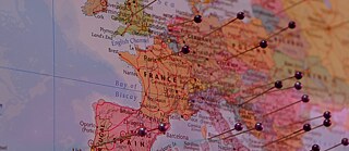 L’image montre un extrait d’une carte imprimée de l’Europe. Les pays au centre de l’image sont la France, les pays du Benelux, l’Allemagne, le nord de l’Italie et une partie de l’Espagne. Plusieurs noms de villes et de pays sont visibles, notamment Paris, Londres, Bruxelles, Amsterdam, Bordeaux, Marseille, Barcelone et Madrid. De nombreuses punaises de couleur à tête ronde sont fixées sur la carte.