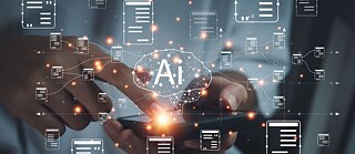 Symbolbild für Künstliche Intelligenz: Eine Hand berührt mit dem Finger ein Smartphone, verschiedene symbolische Nachrichten erscheinen im Vordergrund. Mittig ein angedeutetes Gehirn mit den Buchstaben "AI" für Artificial Intelligence.