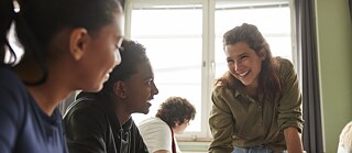 Schüler arbeiten in Gruppen im Klassenzimmer, während die Lehrerin lacht und sie ermutigt.
