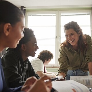 Schüler arbeiten in Gruppen im Klassenzimmer, während die Lehrerin lacht und sie ermutigt.