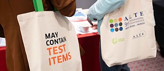 Zwei Konferenzteilnehmende tragen Jutebeutel mit dem Logo der ALTE-Konferenz und der Aufschrift „May contain test items“.